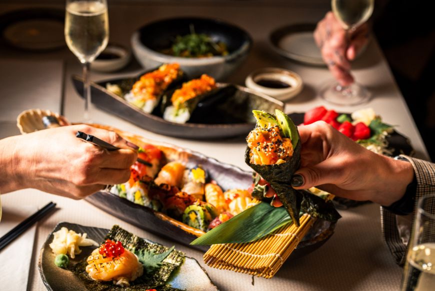 a table of japanese food and drinks, and people digging in